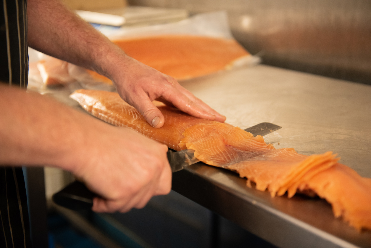 Fresh salmon being sliced on a work surface during food preparation.