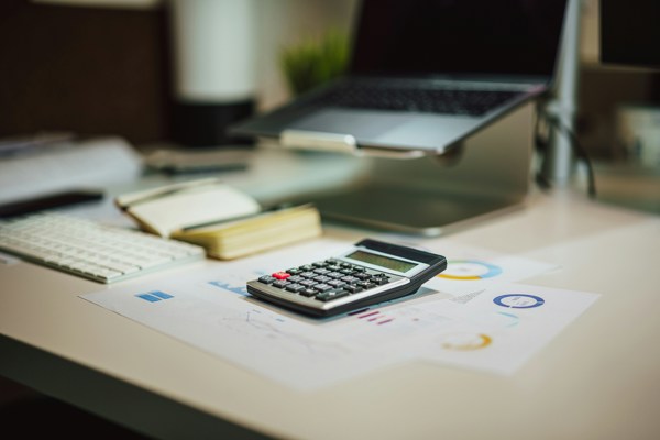 Calculator on financial documents alongside a laptop, keyboard and notebook on an office desk.