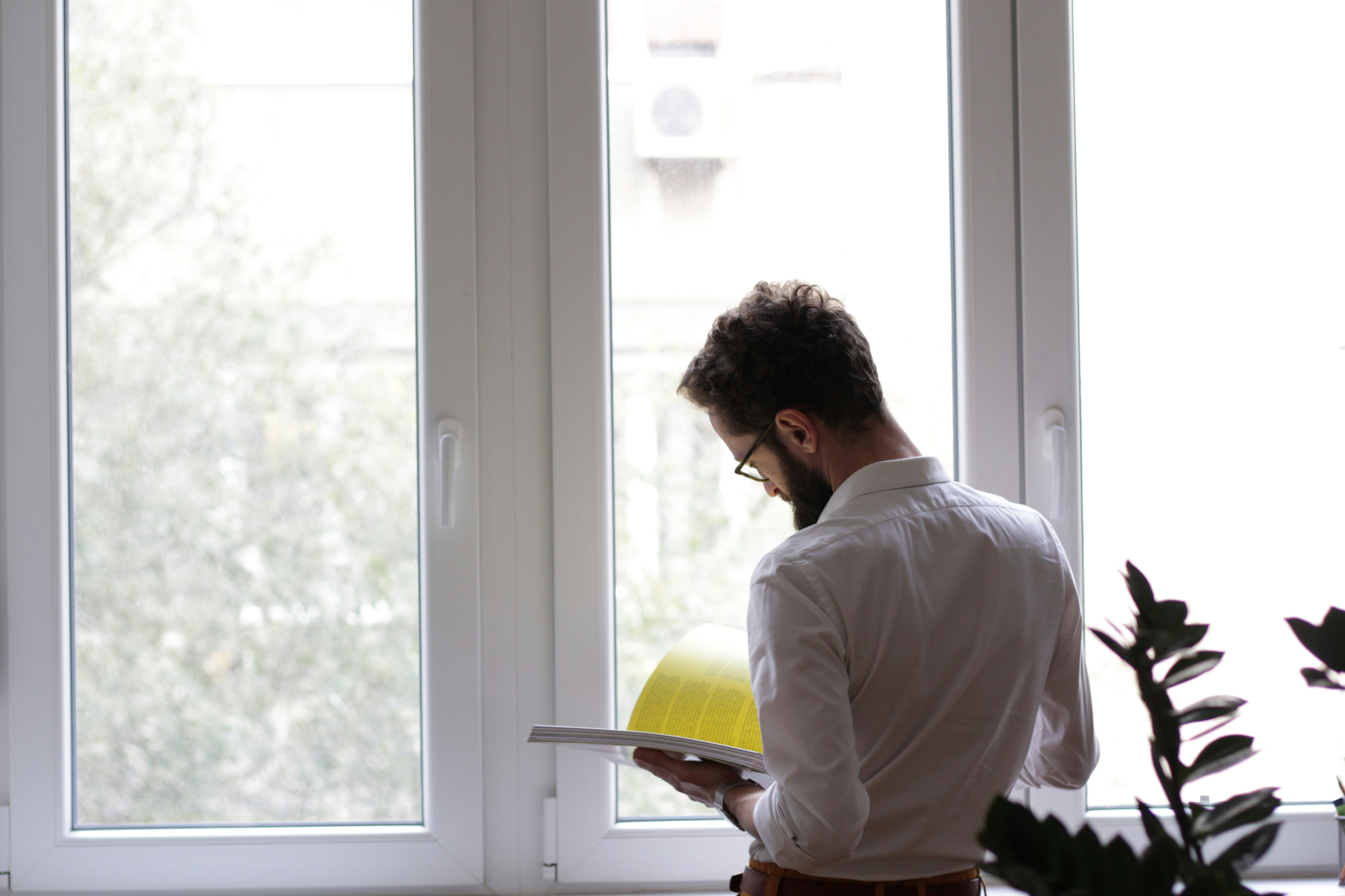 Person standing beside a large window reading a document inside a residential property, illustrating property inspection, housing management and landlord compliance responsibilities.