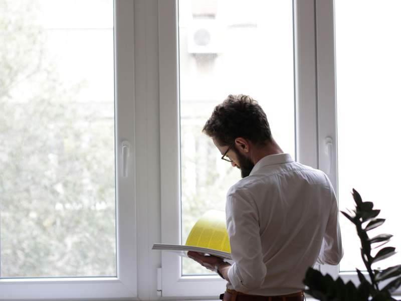 Person standing beside a large window reading a document inside a residential property, illustrating property inspection, housing management and landlord compliance responsibilities.