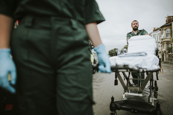 Ambulance workers in uniform moving a patient on a stretcher outdoors in a residential area.