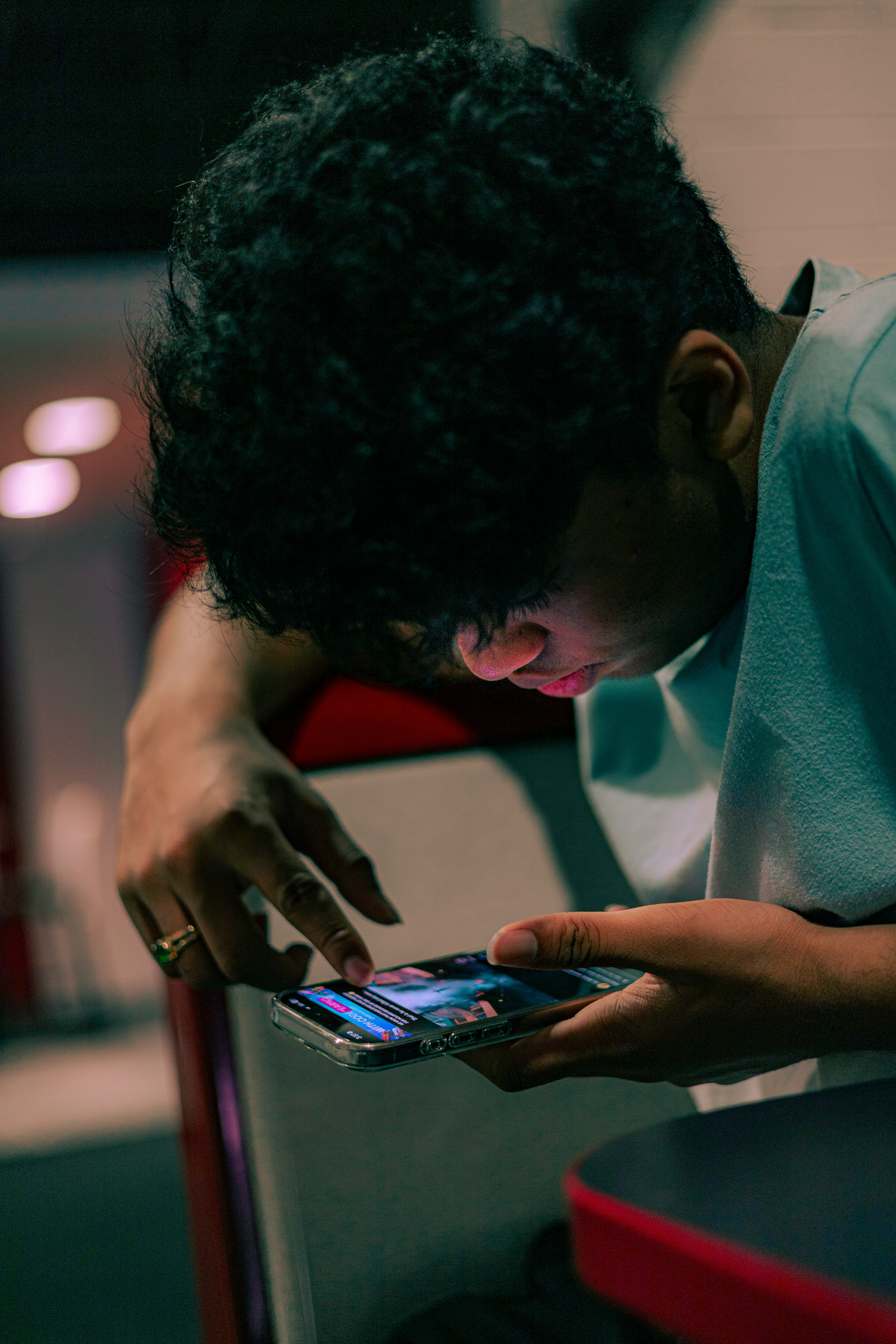 Young person using a smartphone in a low-lit environment, representing online services, digital content access and age assurance in the online environment.
