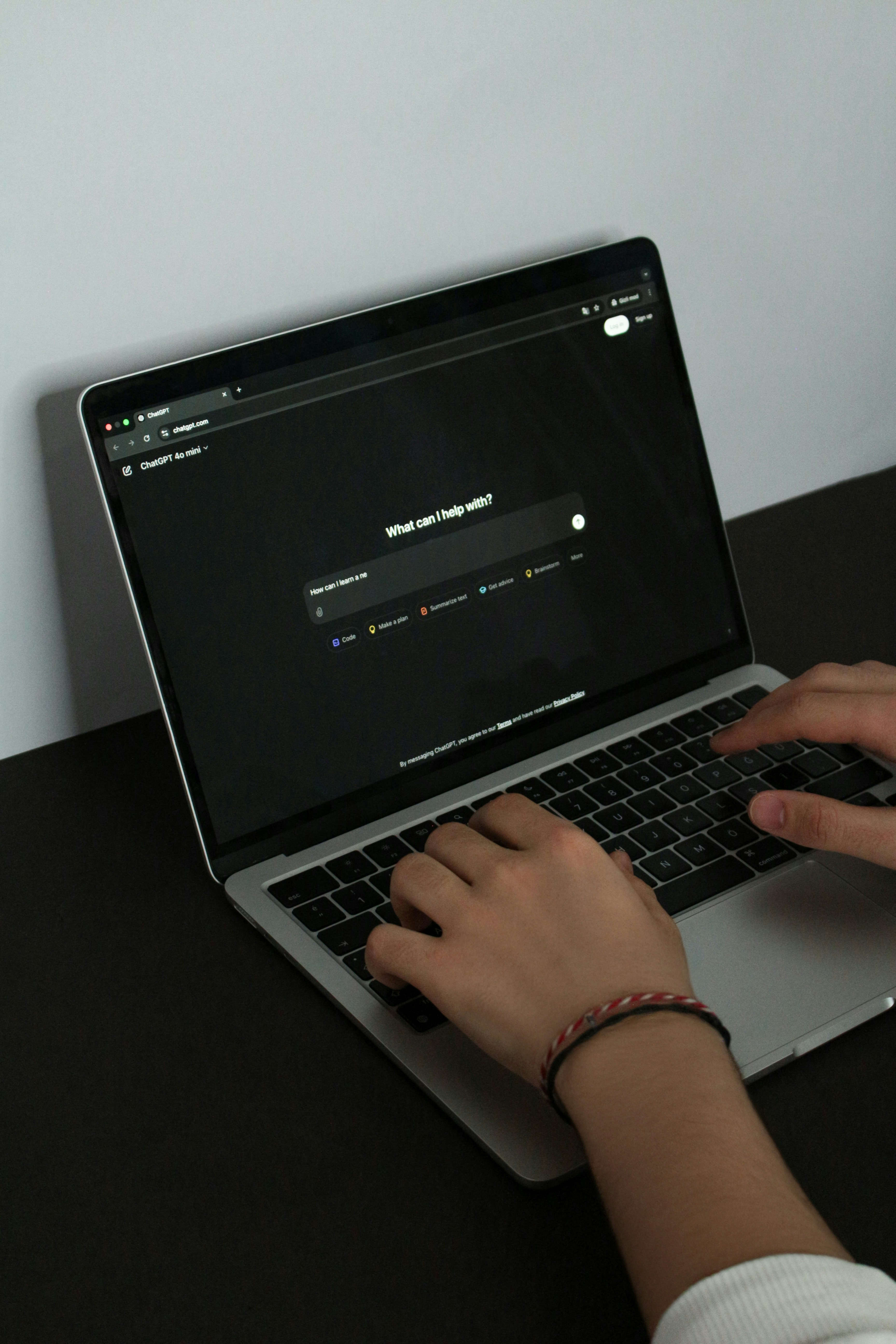 Hands typing on a laptop displaying an AI-powered search interface on a dark screen, placed on a desk.