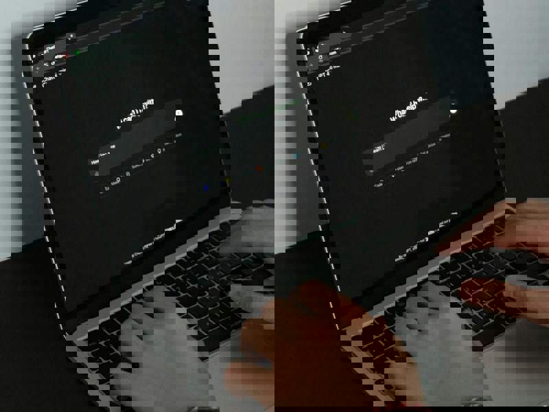 Hands typing on a laptop displaying an AI-powered search interface on a dark screen, placed on a desk.