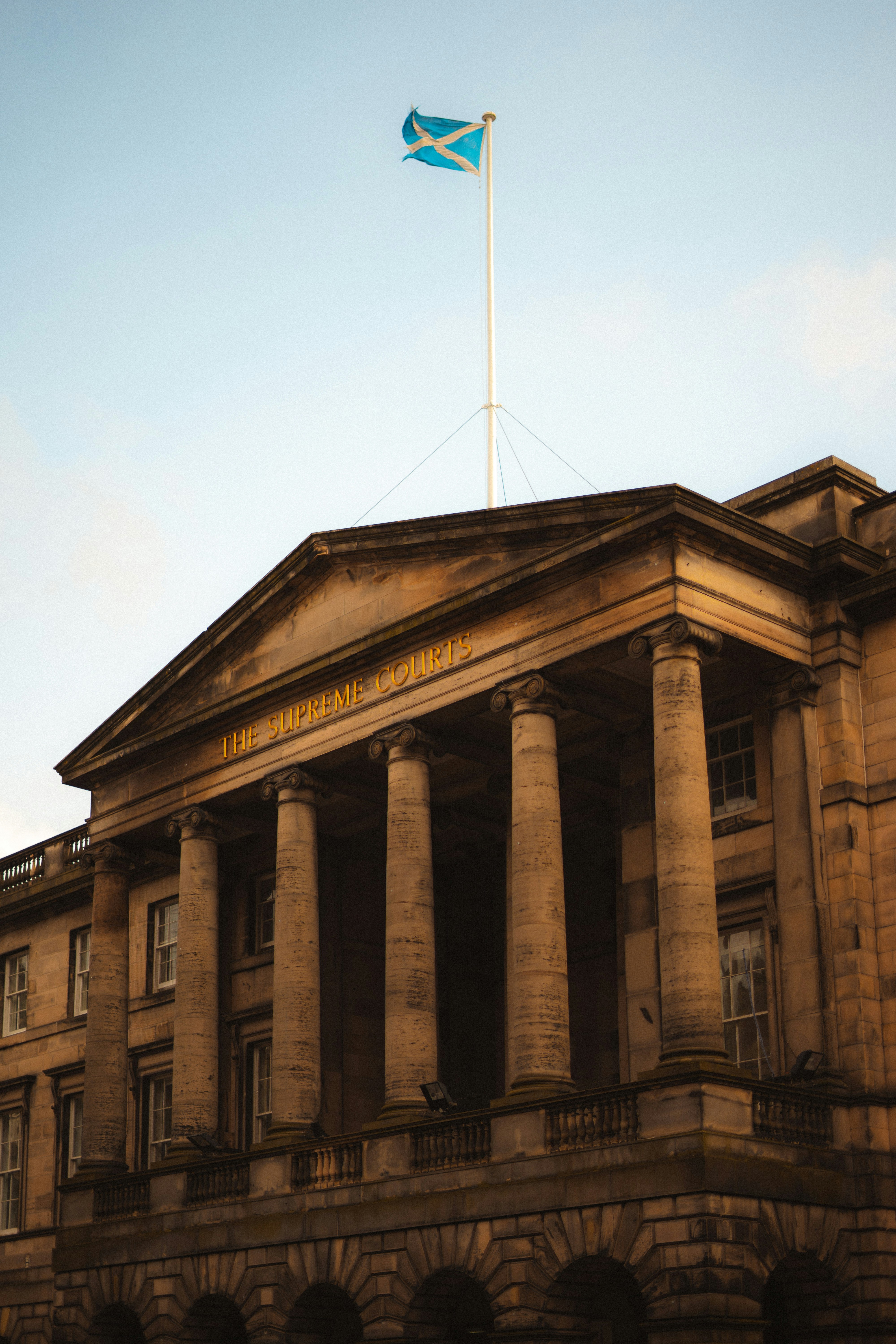 The Supreme Courts building in Edinburgh with classical stone columns and the Scottish flag flying above, representing the Scottish legal system and judicial decision-making.