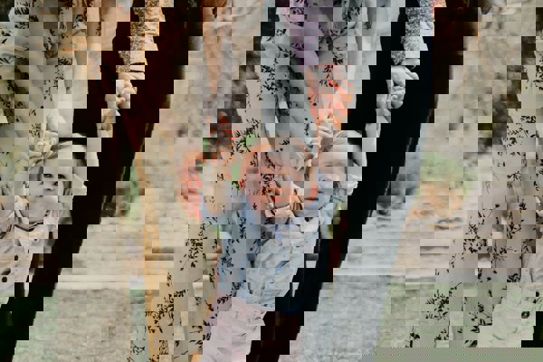  Two adults holding a young child’s hands while walking outdoors on a grassy area, symbolizing family connection and support. The adults are dressed in patterned and dark clothing, and the child is wearing a light blue shirt and pink trousers.