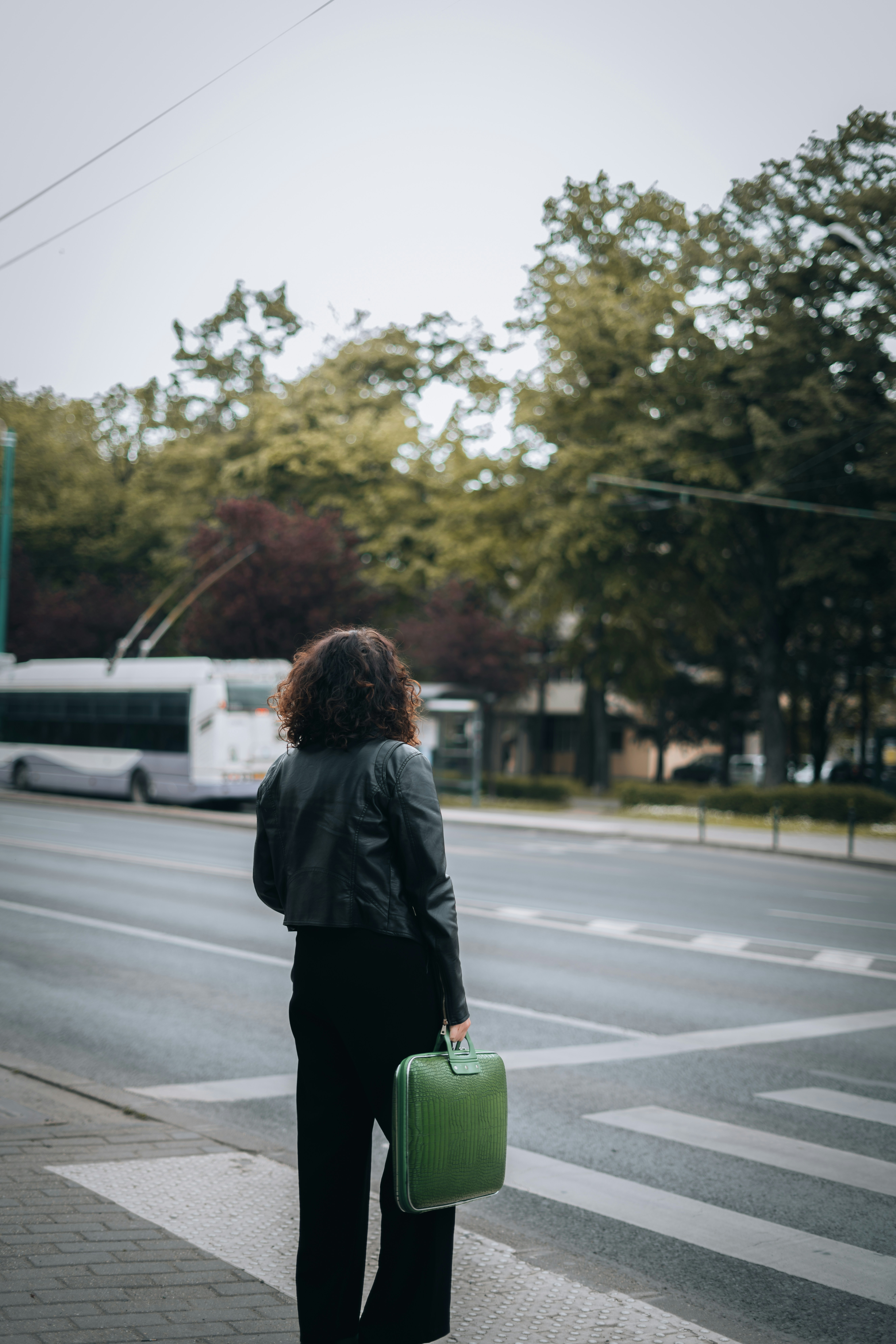 A person stands at a zebra crossing holding a green handbag, facing an empty road with a bus in the distance and trees in the background. The image symbolises being at a crossroads, reflecting the consequences of concealing secondary employment and the uncertainty that follows dismissal.