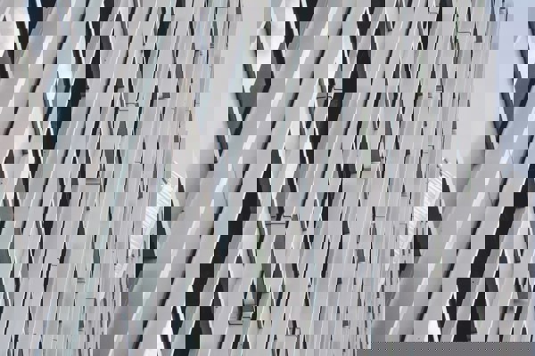 Close-up view of a modern building façade with repeating vertical and diagonal metal panels forming a geometric pattern against a pale sky.