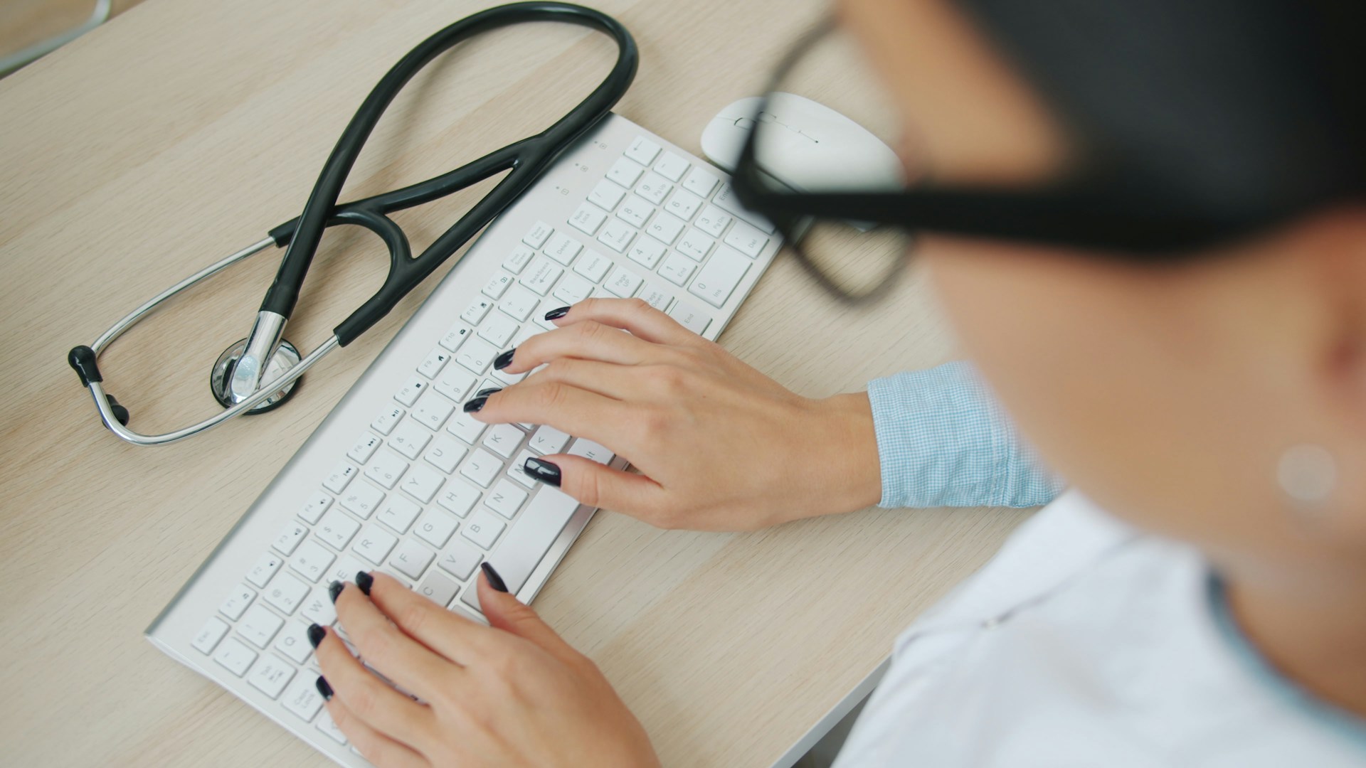 Healthcare professional using a computer, with a stethoscope resting on a desk beside a keyboard.