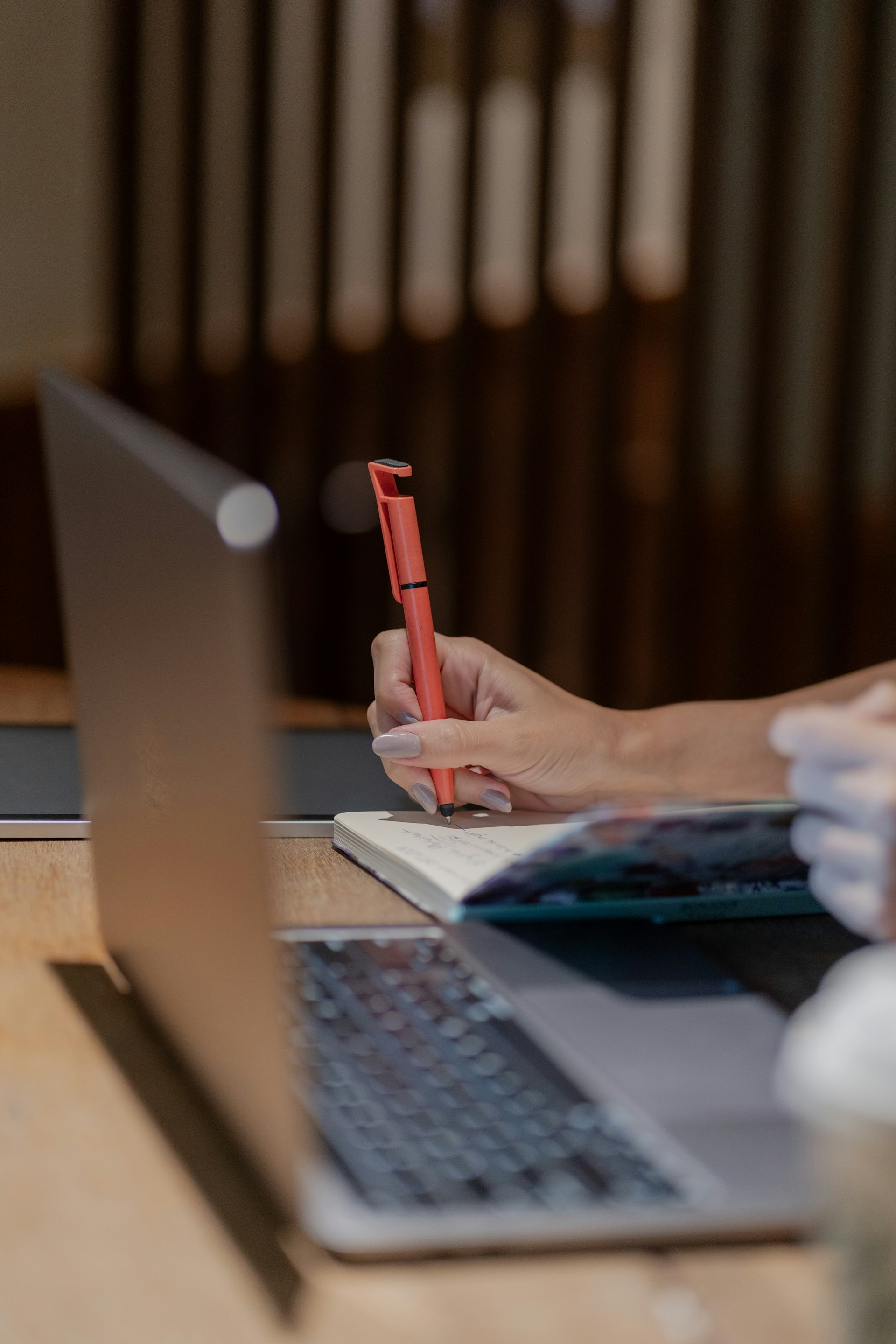 A person taking handwritten notes in a notebook beside an open laptop, suggesting human review and analysis.