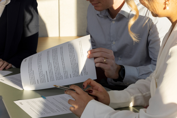 Multiple people at a desk reviewing printed guideline documents, holding papers and a pen while discussing revisions.