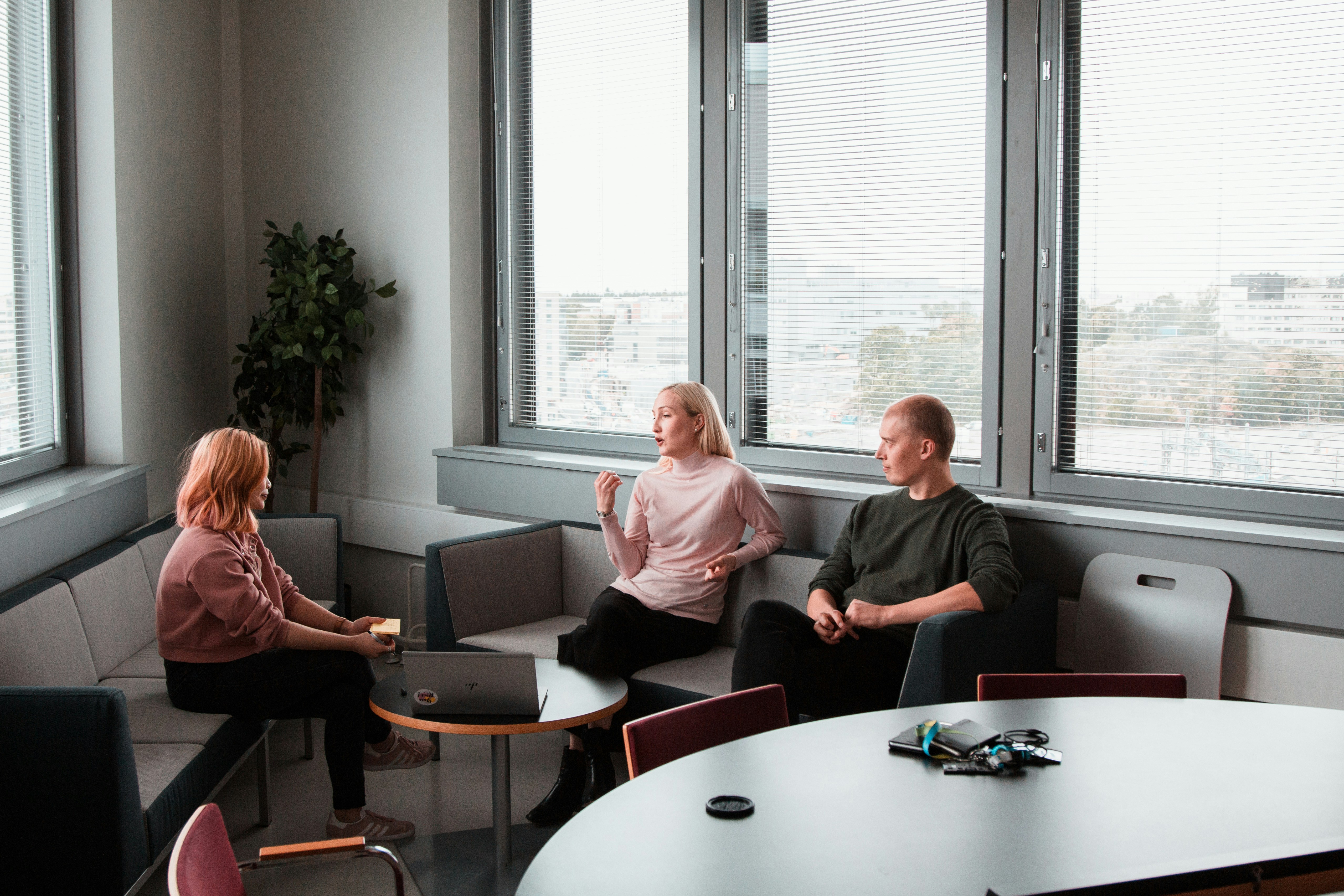 Group of people seated in a modern meeting space, engaged in discussion around a table.