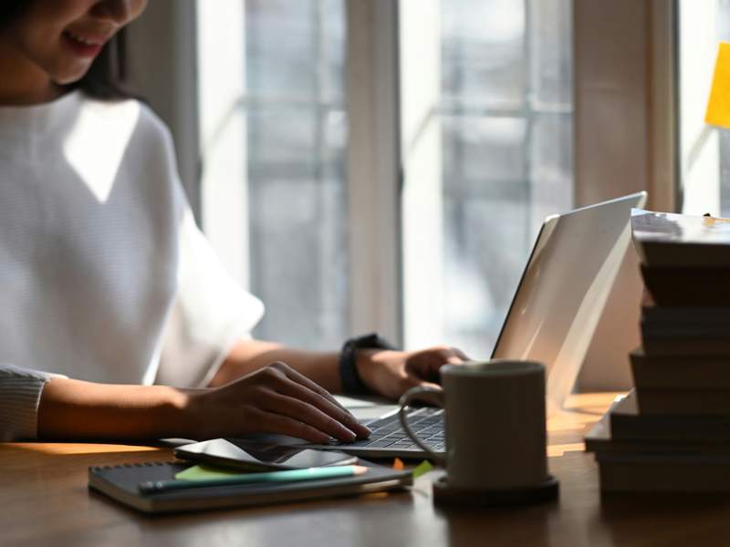Person writing on a laptop beside books and notes, illustrating the creation of original content and intellectual property.