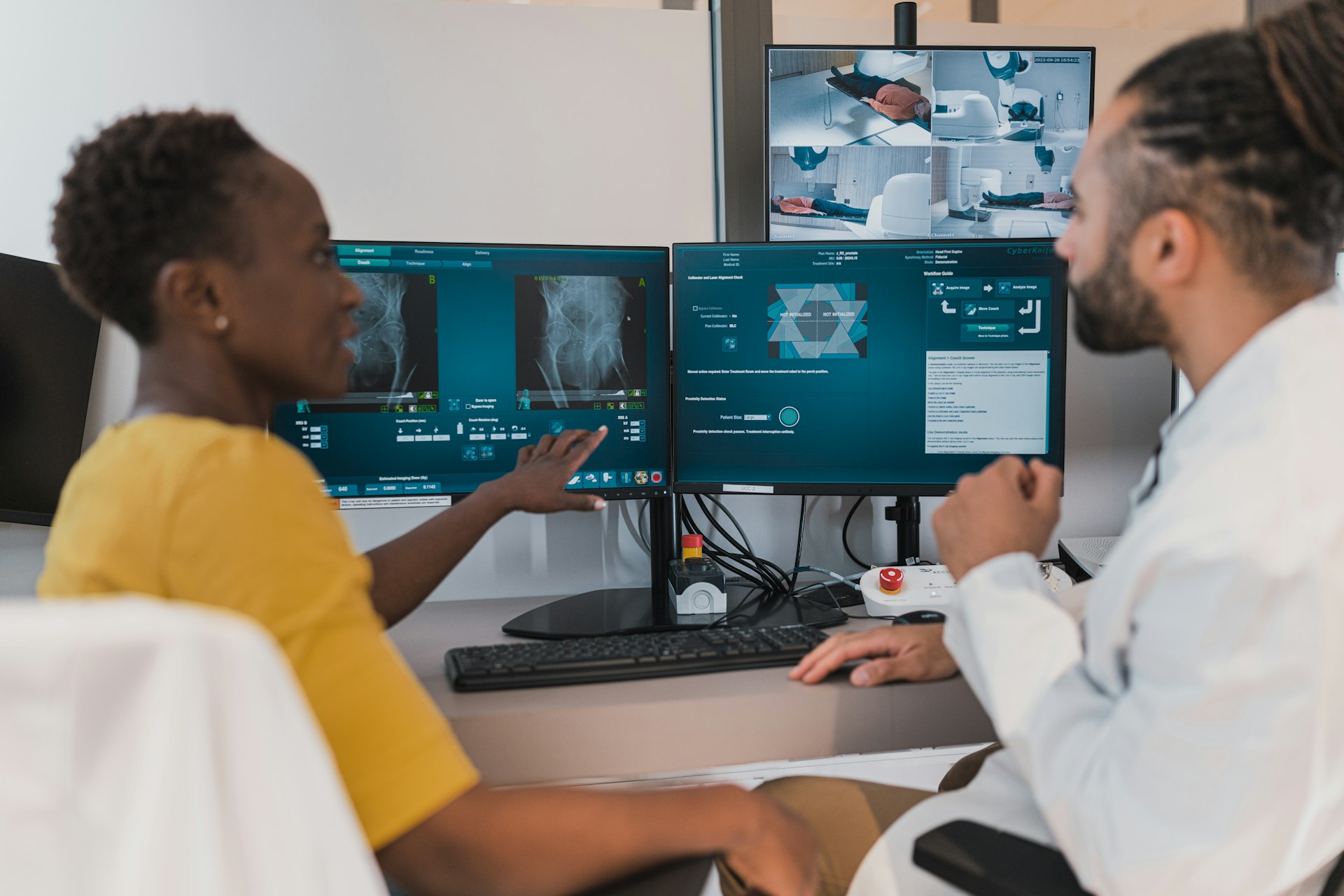 Healthcare professionals review medical imaging and patient data on multiple digital monitors displaying X-rays, treatment information and healthcare technology dashboards.