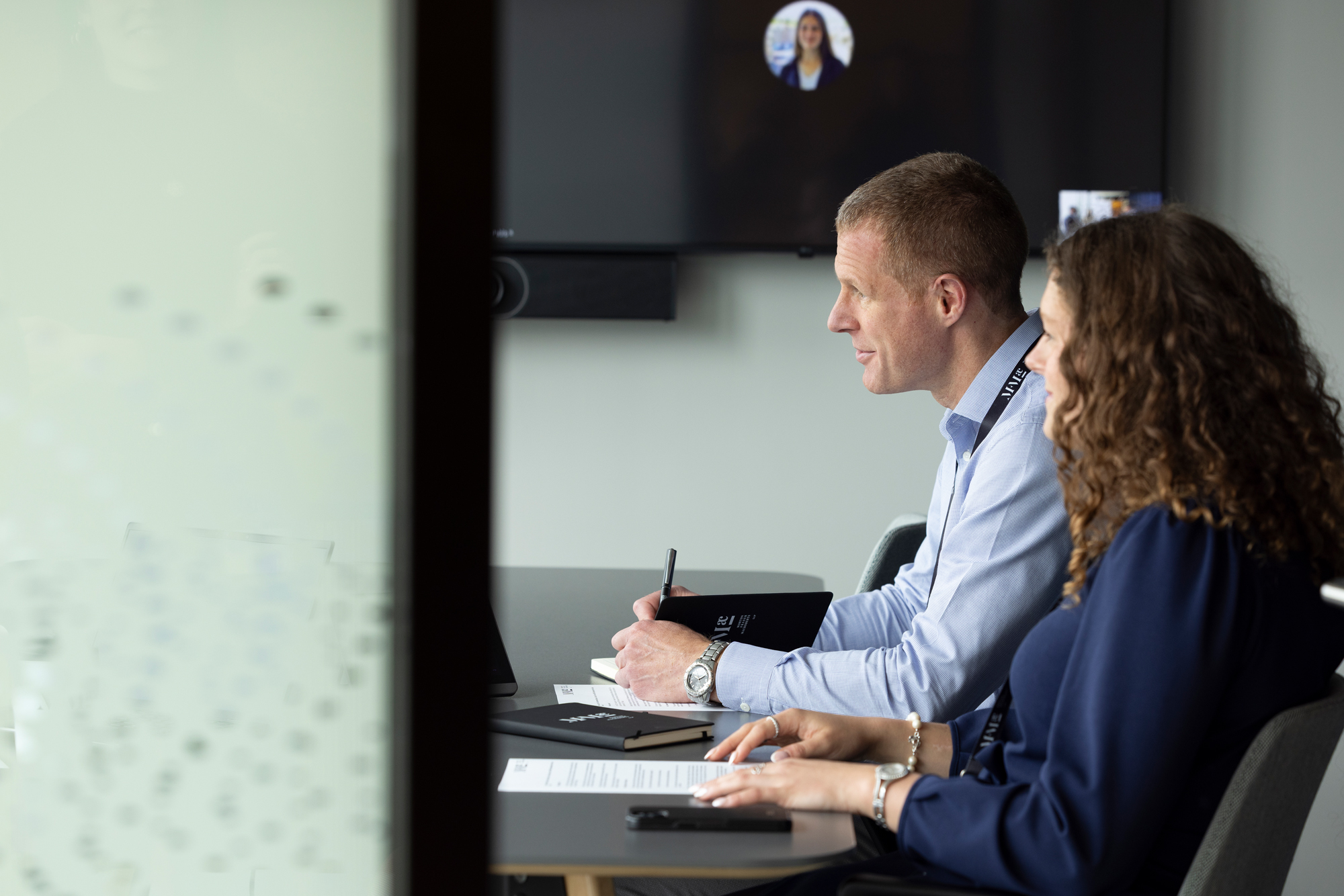 Two professionals seated in a meeting room reviewing documents and taking notes during a business discussion.