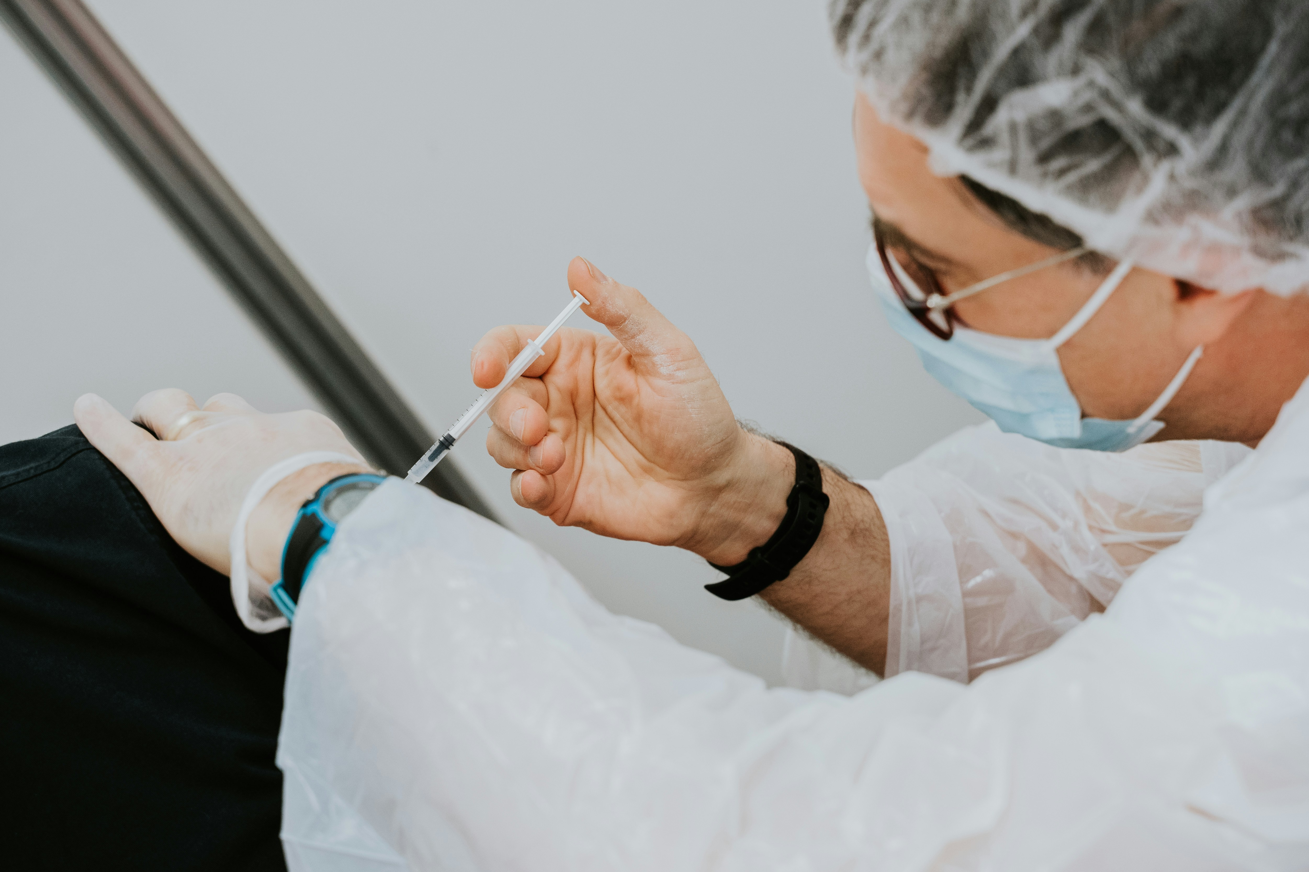Practitioner administering a cosmetic injection in a clinical setting using protective gloves and mask.