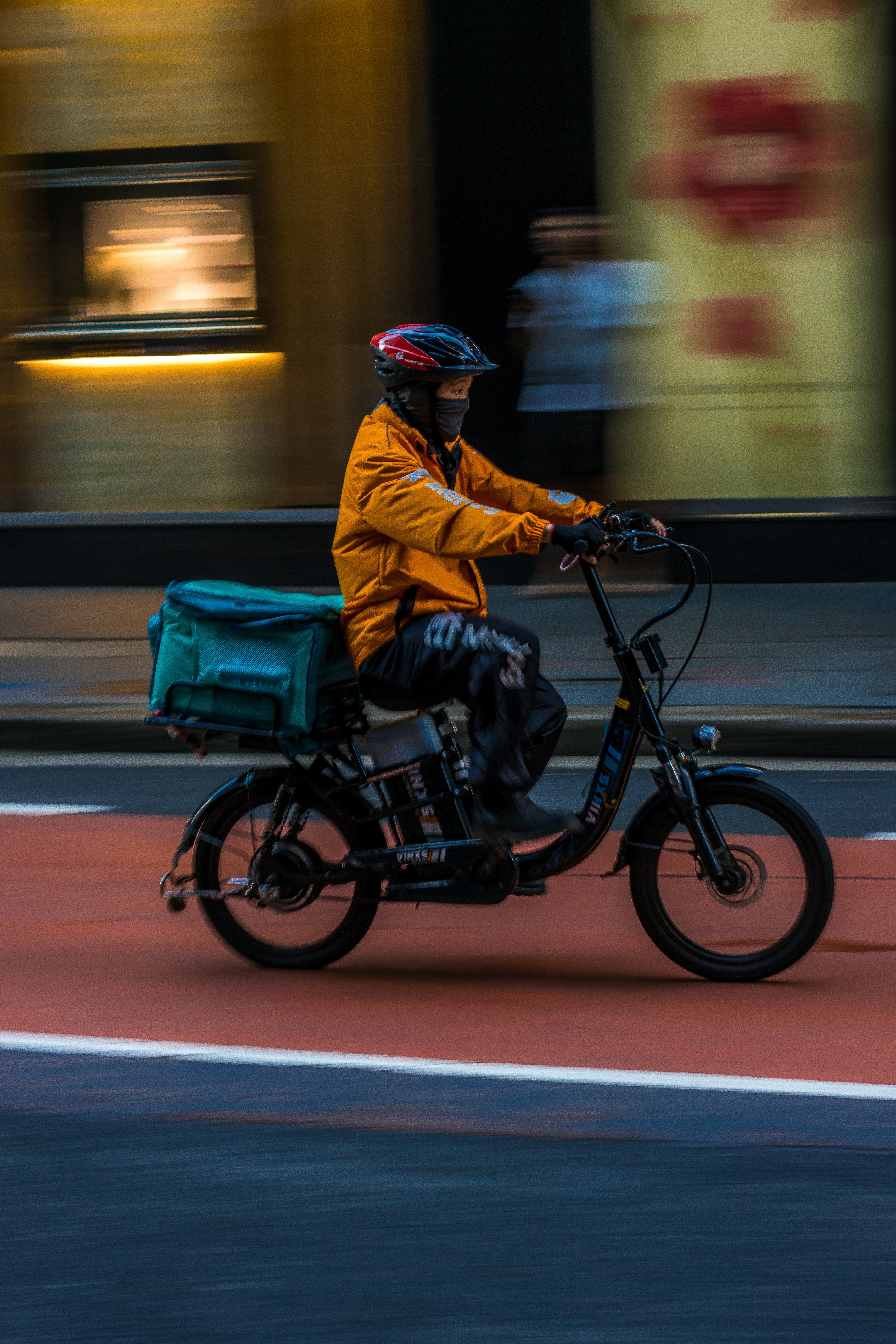 Delivery rider on an e-bike travelling through a city street with a delivery bag mounted on the rear.