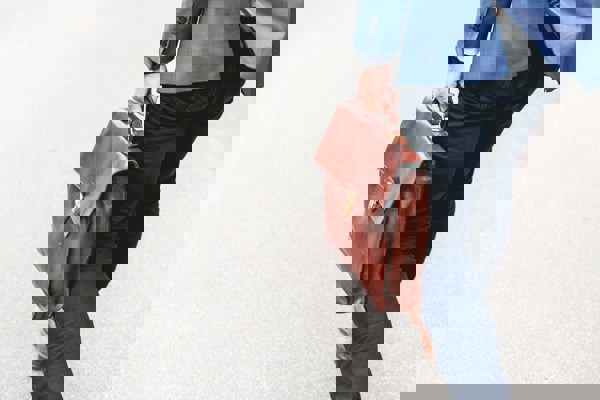 A person in business attire walking away on a pavement while carrying a brown leather briefcase, symbolizing job loss or departure due to redundancy.