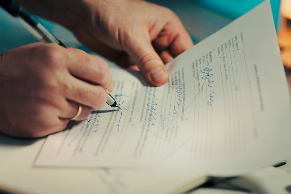 Close-up of hands signing a printed legal document with a pen, illustrating the preparation and execution of formal written notices.