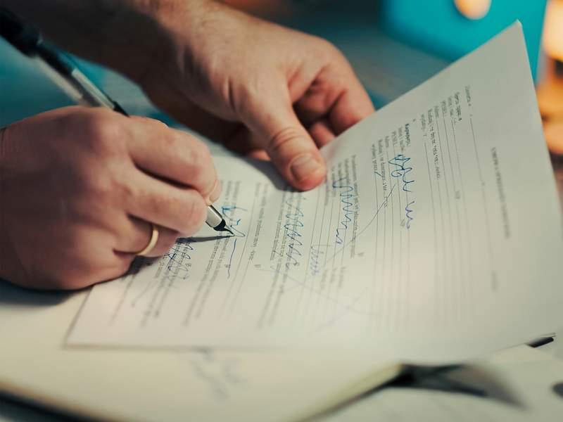 Close-up of hands signing a printed legal document with a pen, illustrating the preparation and execution of formal written notices.