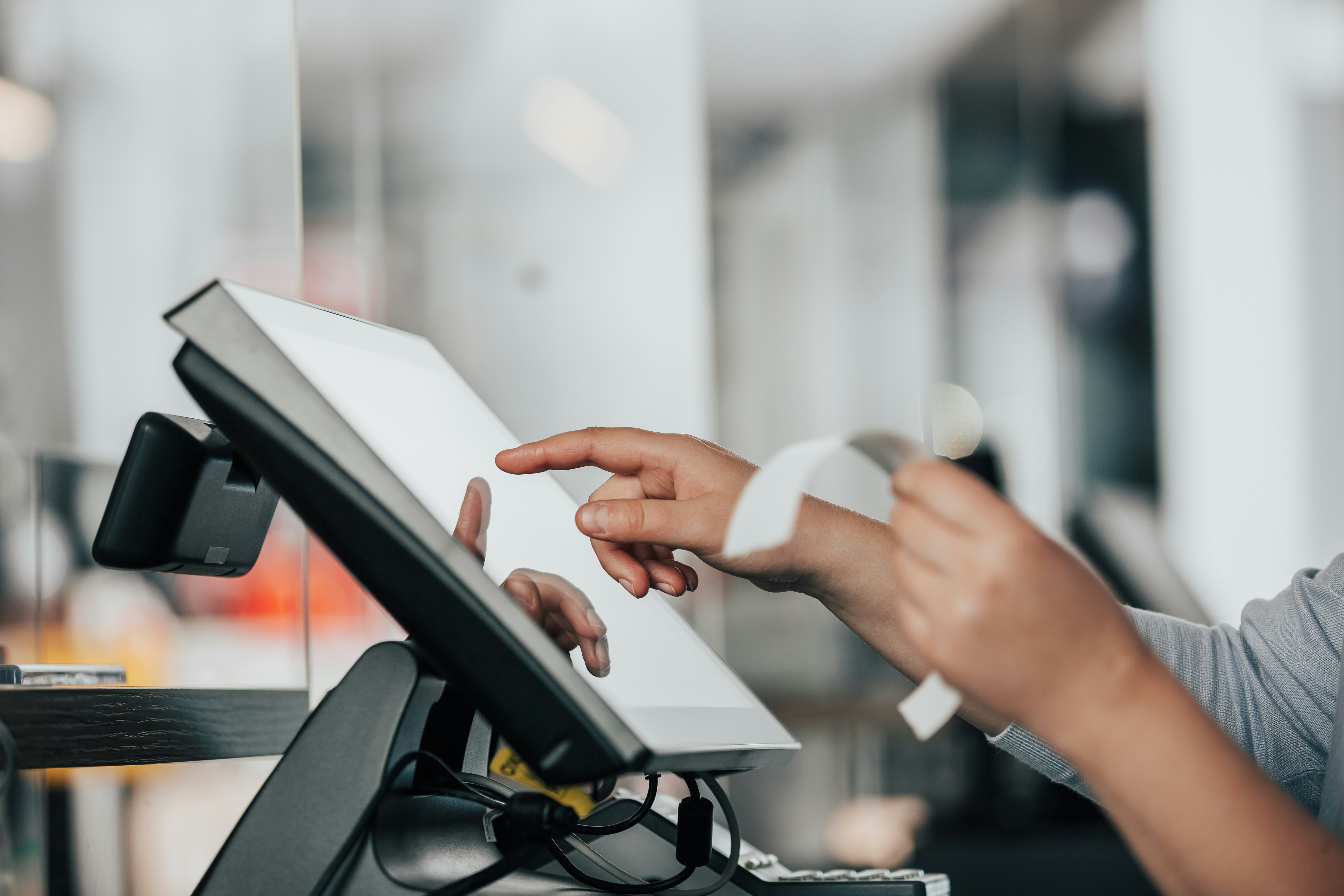 Person using a touchscreen till at a retail checkout, holding a printed receipt.