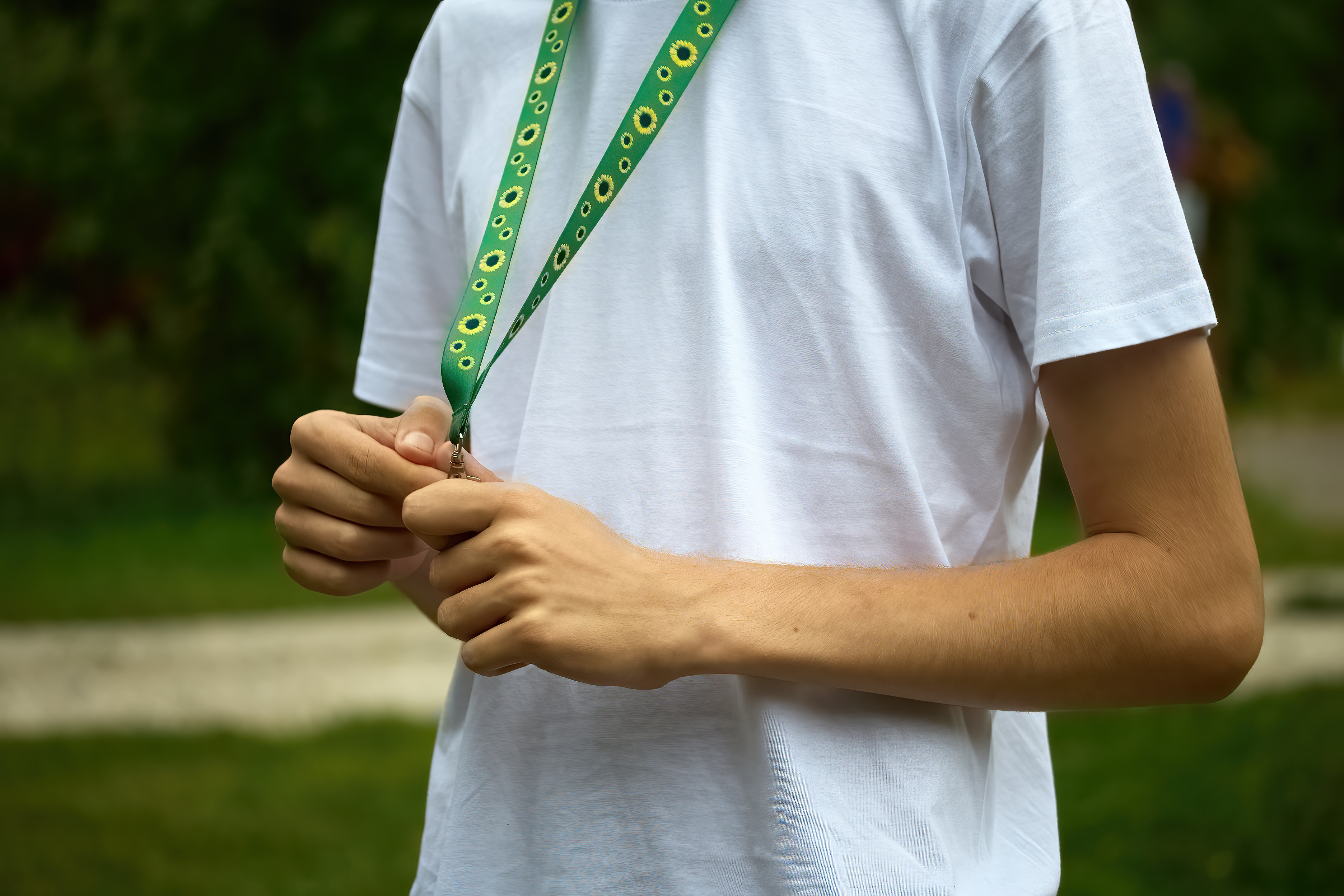 Person wearing an ID lanyard, adjusting the badge while standing outdoors.