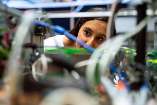 Close-up of a person working with electronic components and wiring, viewed through blurred cables and equipment.