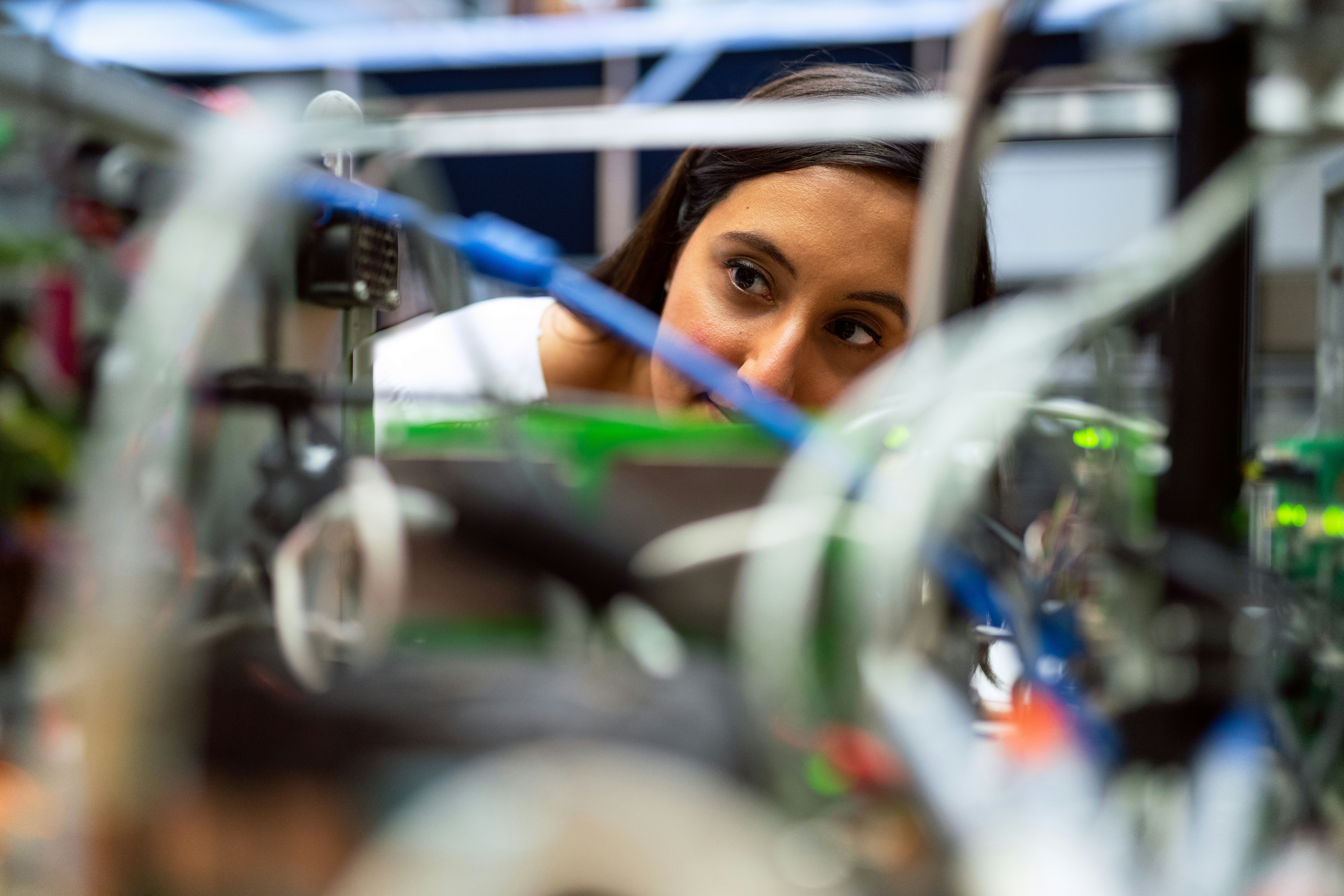 Close-up of a person working with electronic components and wiring, viewed through blurred cables and equipment.