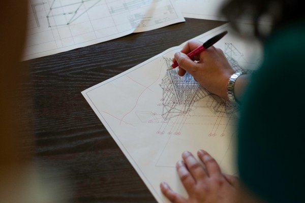 Person reviewing and marking up architectural drawings and technical plans on a desk during the design phase of a construction project.