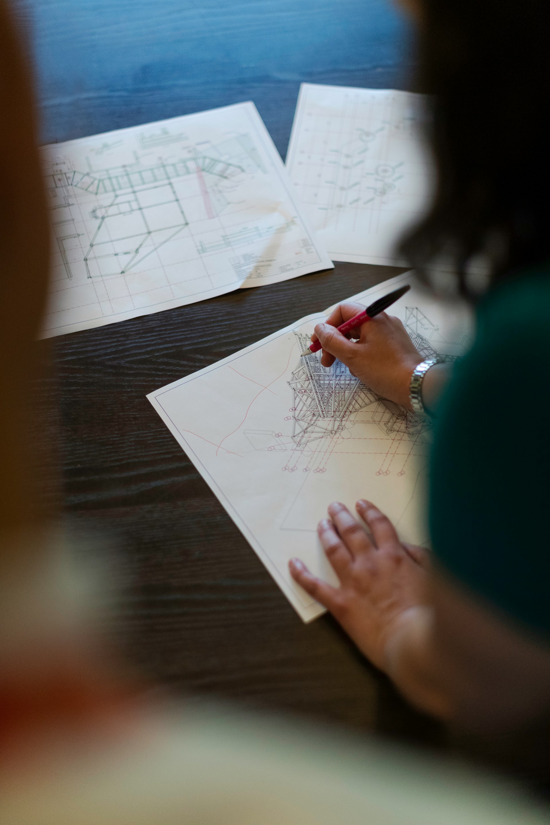 Person reviewing and marking up architectural drawings and technical plans on a desk during the design phase of a construction project.
