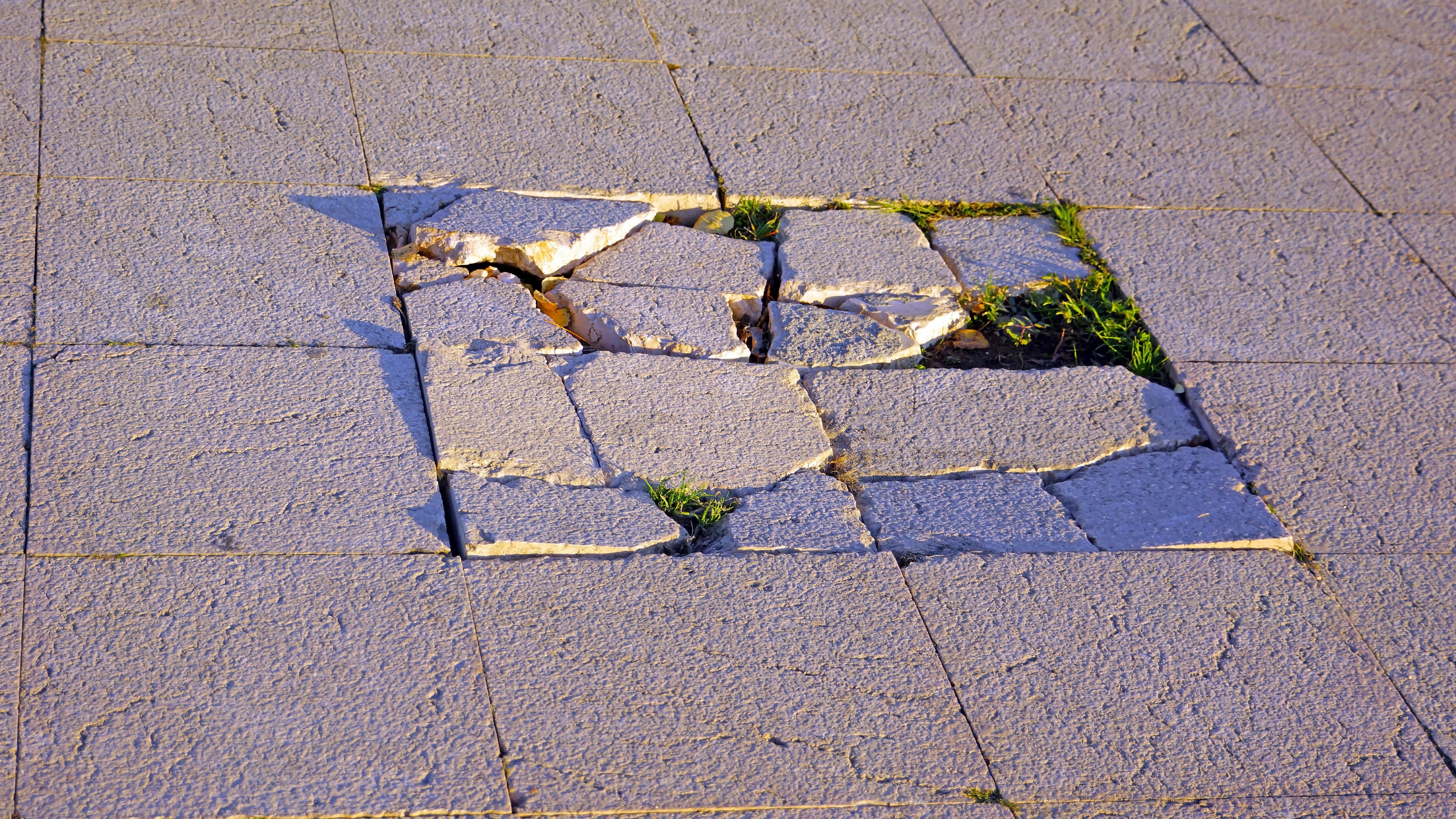 Broken and uneven paving slabs creating a trip hazard on a public pavement.