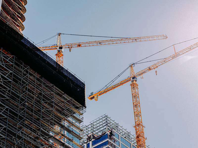 Tower cranes and scaffolding around a large construction project, illustrating the construction sector and project delivery risks.
