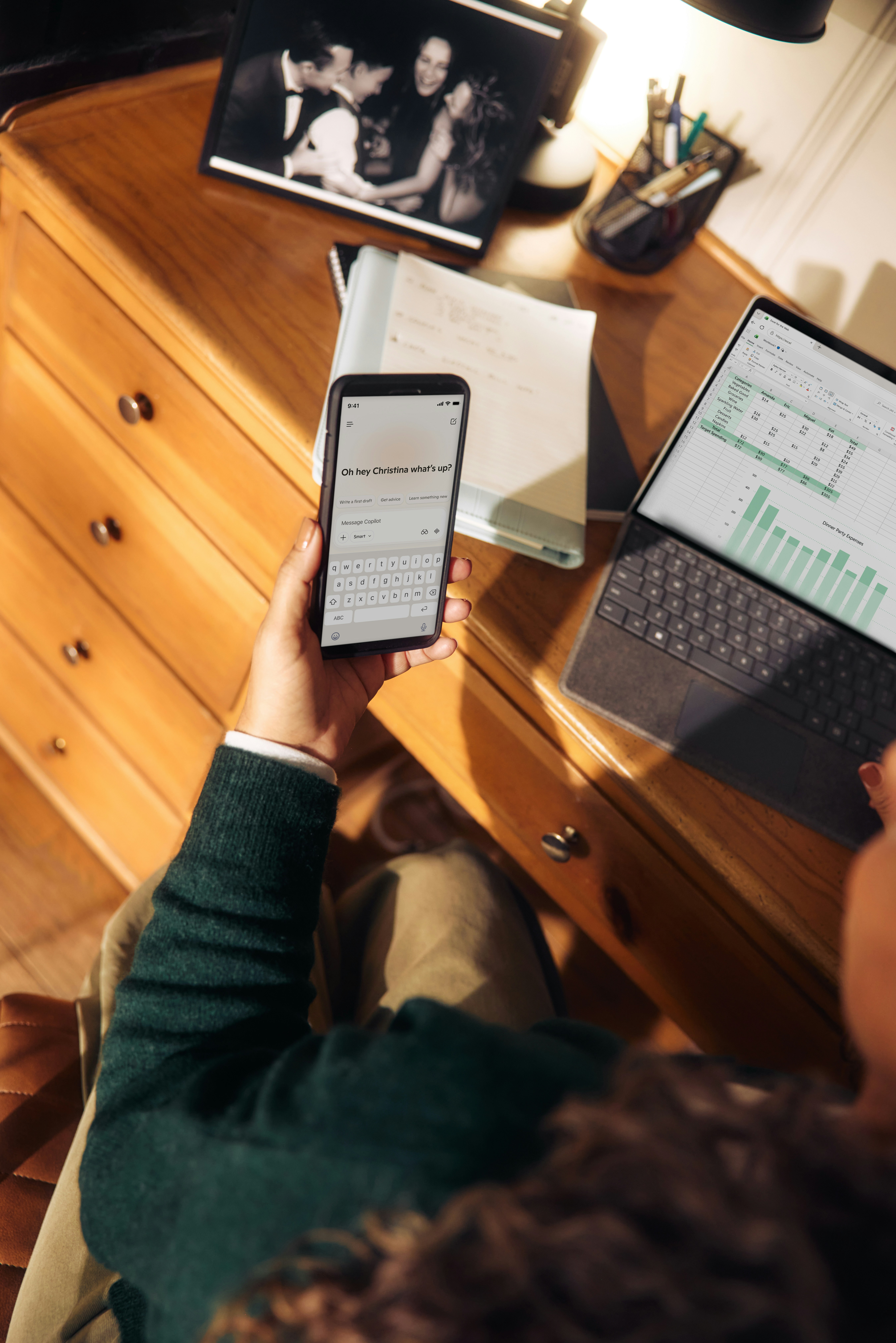 Person working at a wooden desk, holding a smartphone while analysing data on a laptop