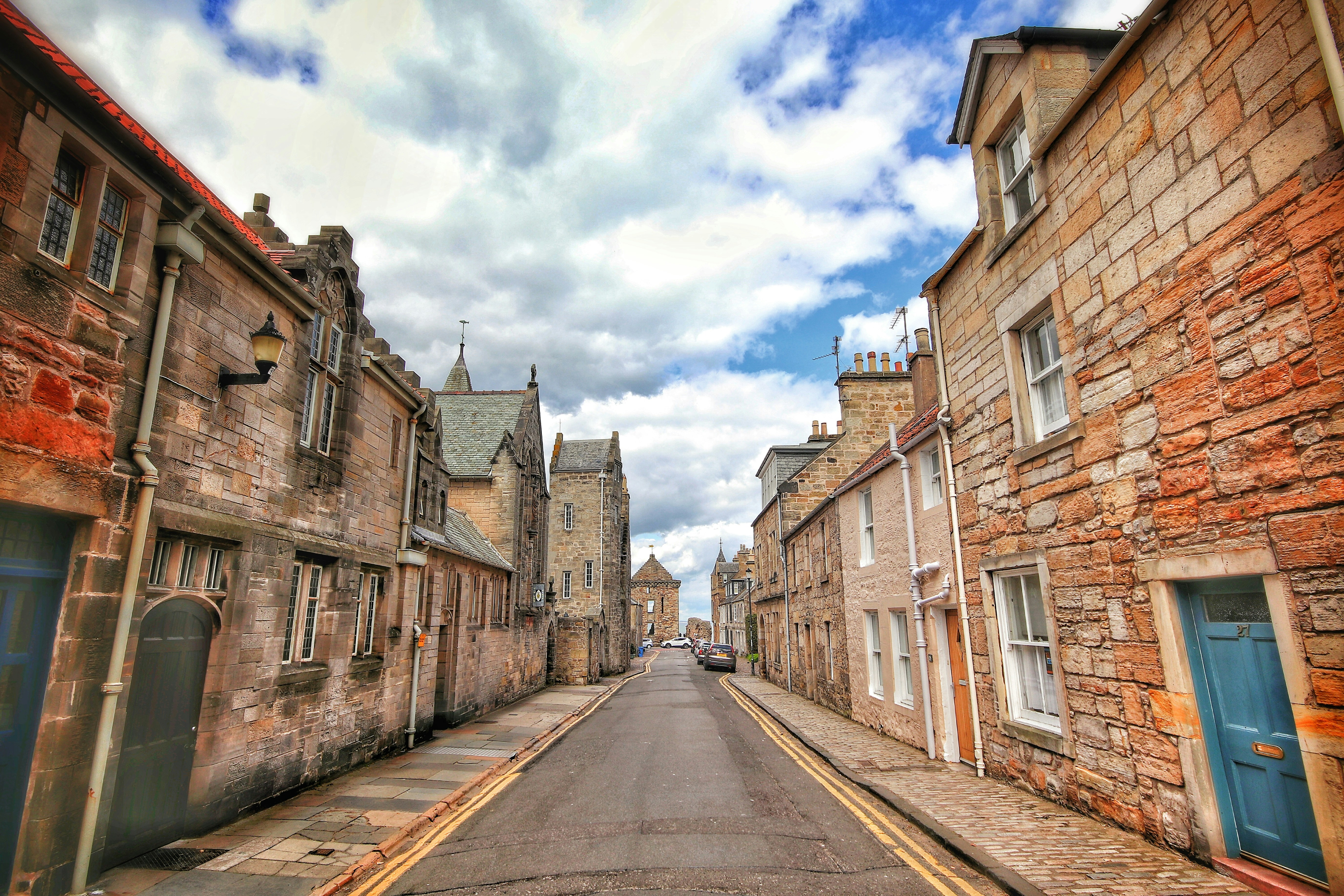 Historic Scottish street lined with traditional stone buildings, viewed from the centre of the road under a cloudy sky