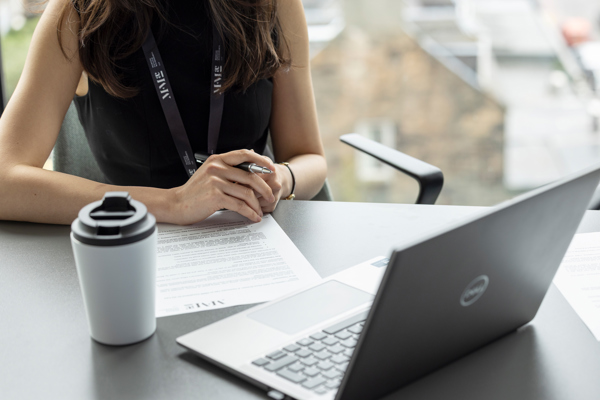Person reviewing printed documents at a desk with a laptop and notebook in a modern office setting.