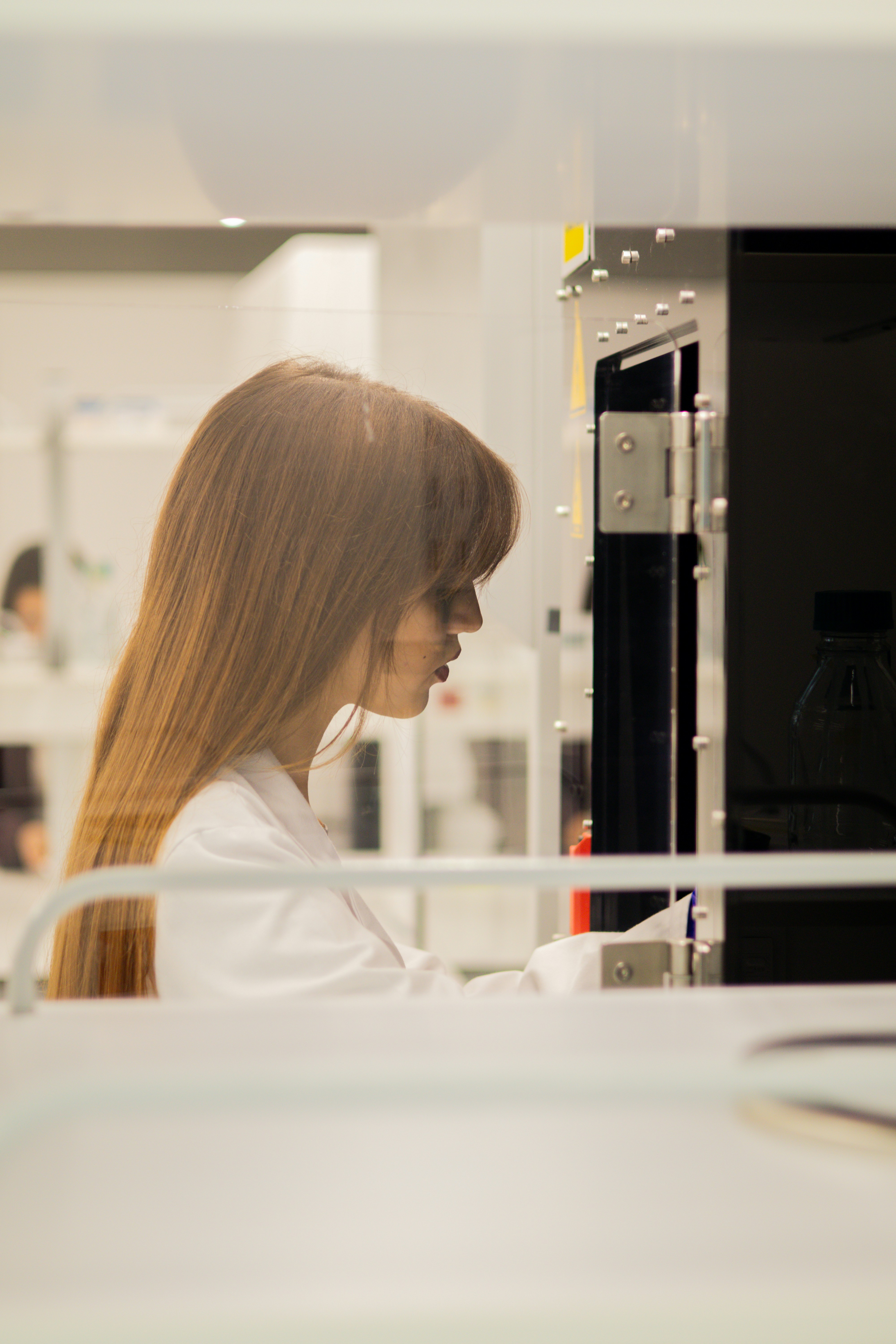 Person in a laboratory environment operating scientific equipment behind a glass partition.
